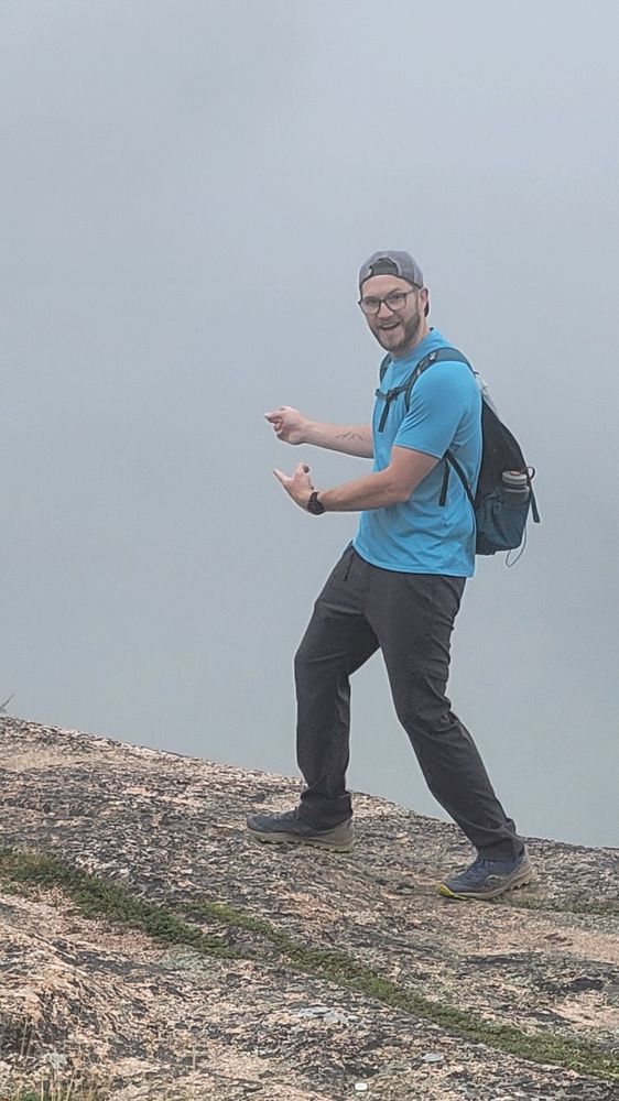 Mac is standing on a rock pointing at fog.