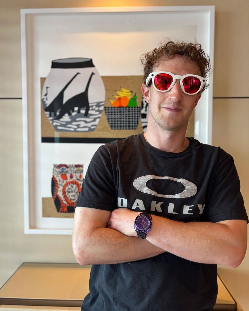 picture of mark zuckerburg in an oakley tshirt with his arms folded across his chest like he's about to drop the shittiest rhymes about staying away from drugs you've ever heard. He's wearing white glasses with red lenses. his hair looks like some starlings are about to nest in it. he looks like he sucks, becaus he does 