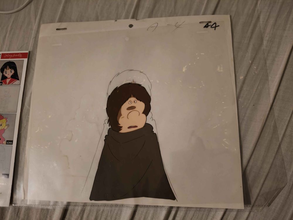 A cel from Galaxy Express 999, depicting the character Tetsuro Hoshino, a boy clad in a brown cloak, with brown hair, a large nose, and two tiny eyes that sit on the top of his forehead, right between where his hair parts.