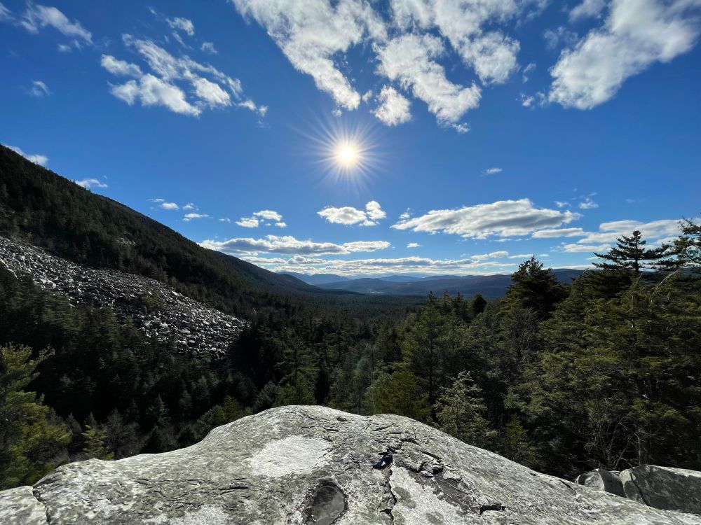 A picture taken from a mountain in the distance the sky is blue with a few clouds and the sun is shining.  