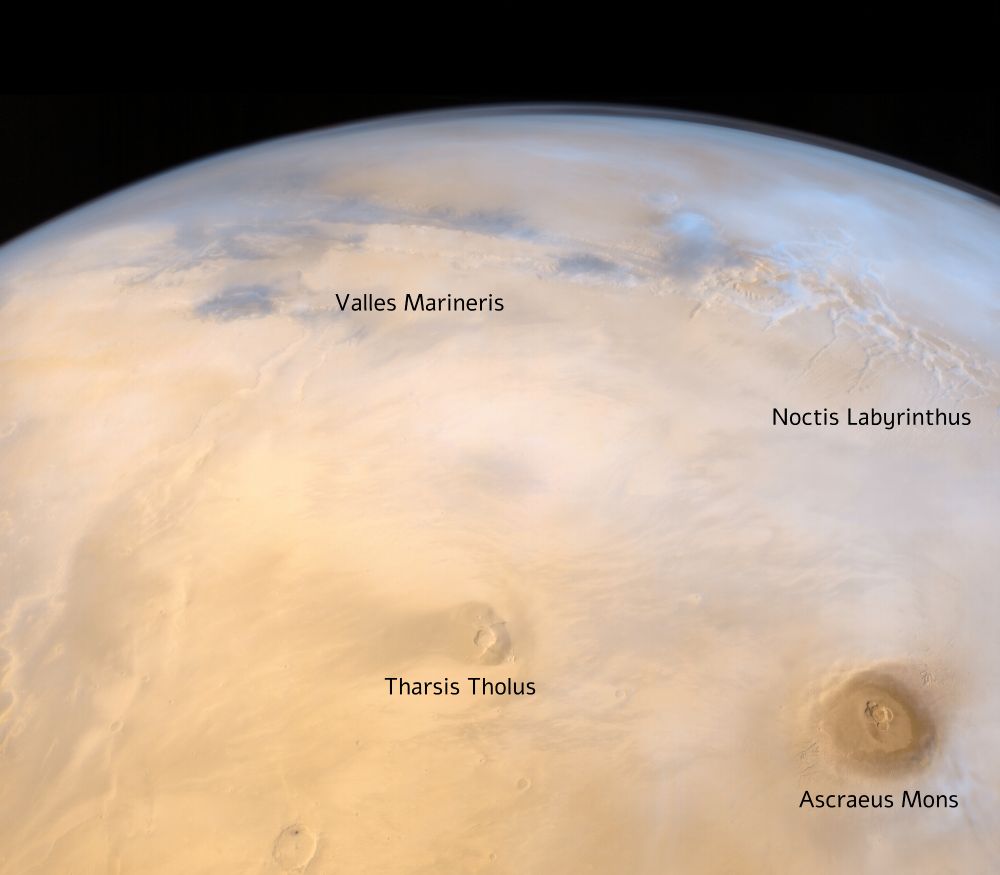 Same image of this thread but with annotations to localize Noctis Labytinthus, Valles Marineris, Tharsis Tholus and Ascraeus Mons marked.

The image shows Mars from space. You can see long, deep canyons with the huge Valles Marineris cutting through the surface. Noctis Labyrinthus looks like a maze of sharp, intersecting valleys. Two large volcanic features stand out, Tharsis Tholus and Ascraeus Mons, with their smooth, cone-like shapes rising from the surrounding. Colours are rusty red on the surface and foggy bluish in the canyons. Along the limb of the planet, a thin layer of atmosphere is visible, just before the darkness of space begins.
