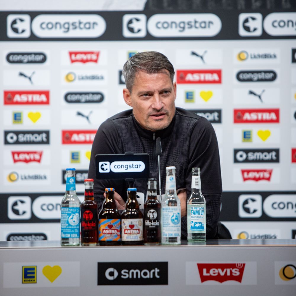 Alexander Blessin sitzt bei einer Pressekonferenz auf dem Podium.