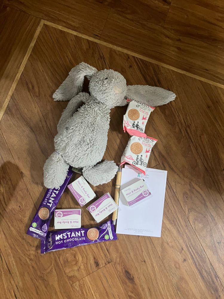 Soft toy rabbit with notebook, pen, soap, hot chocolate sachets and biscuits.