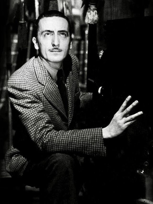 A black and white photo of Italian director Mario Bava wearing a tweed suit and has a moustache. 