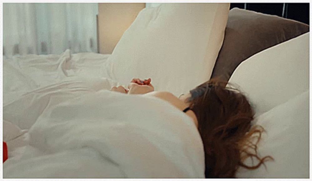 a woman laying in bed with white sheets and pillows