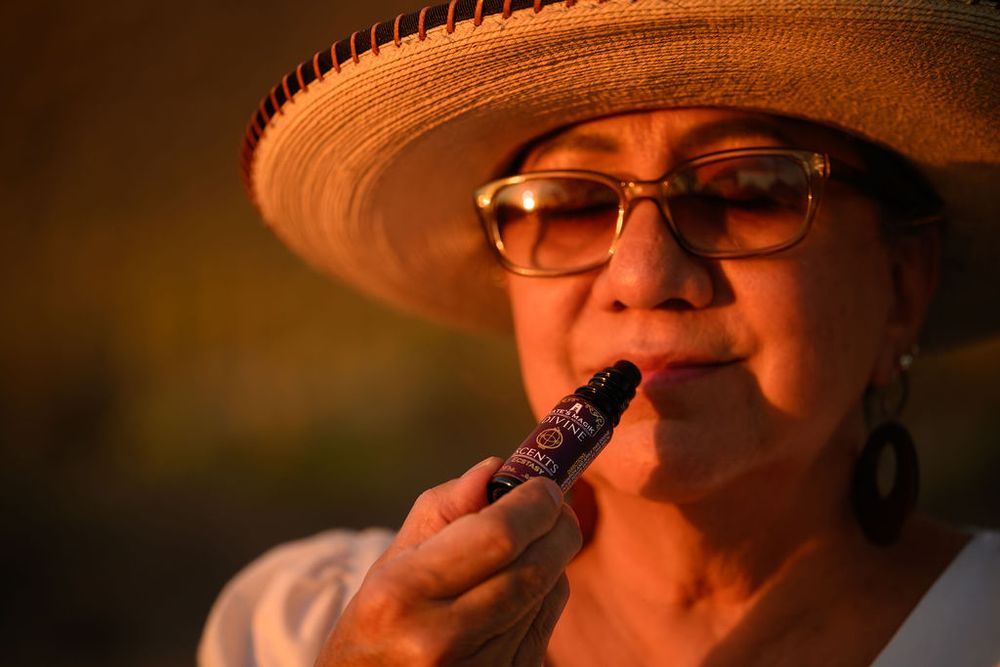 Woman in sun hat, taking a deep breath of the aroma from Kate's Magik Divine Scent Natural Perfume. Taking a moment for breath and aromatherapy, to destimulate in our overstimulated world. With the setting sun shining on her face.
