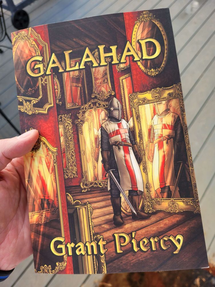A physical copy of GALAHAD by Grant Piercy featuring cover art by Sanrixian, displays a knight in a red cross surcoat facing himself in a hall of ornate mirrors