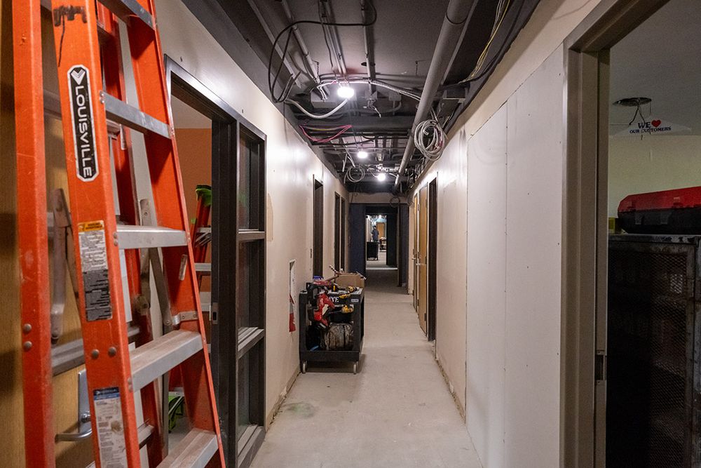 Hallway with open ceiling, electrical wires, and a ladder 