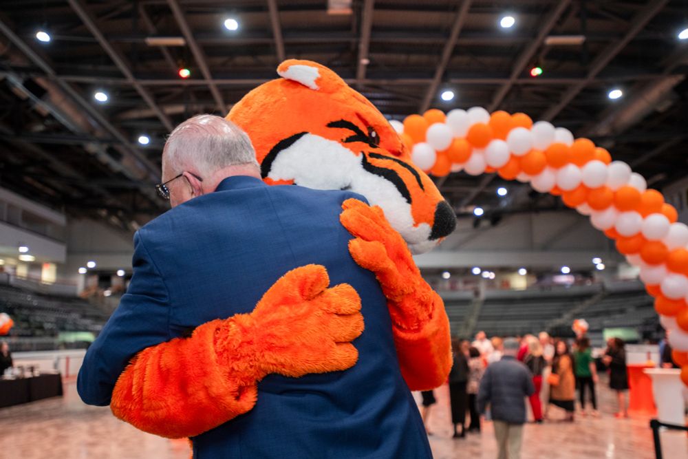 Older man with white hair wearing a suit gives a big hug to Ritchie the tiger mascot