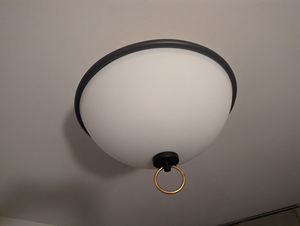 A round ceiling light with a big golden hoop hanging out of the bottom 
