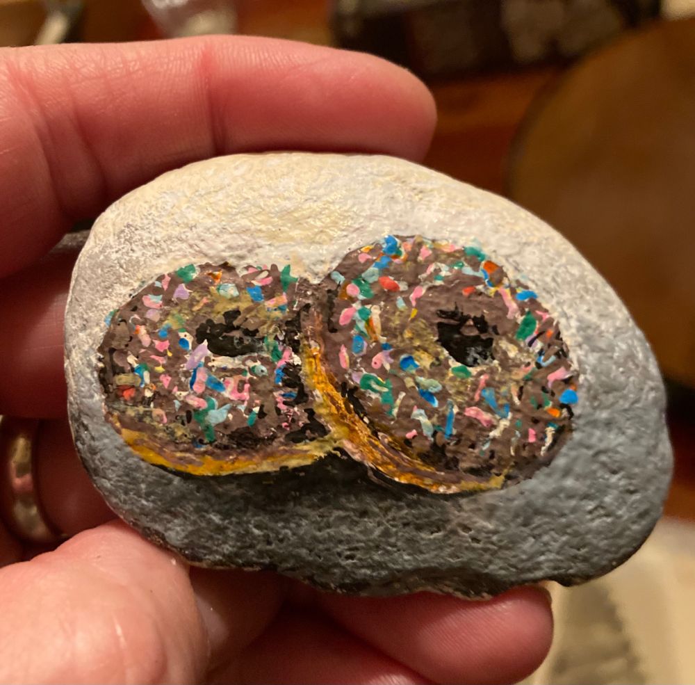 A rock painting of two chocolate-glazed donuts with sprinkles. Yum!
