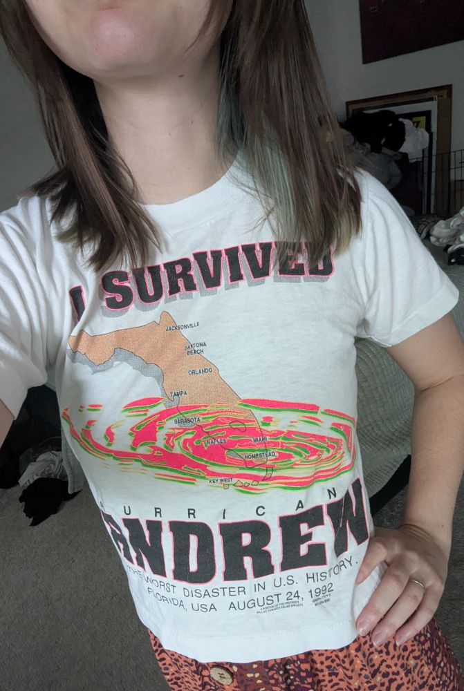 The shirt has a map of Florida with hurricane indicators over it and says "I SURVIVED HURRICANE ANDREW"