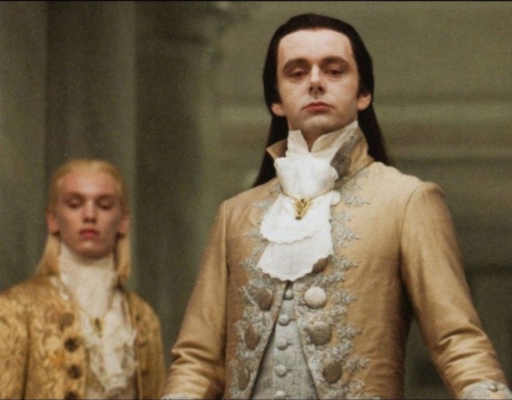 Aro aus der Twilight Saga in festlichem gold schimmerndem Gewand, der herablassend hinab blickt. im Hintergrund eine weitere herablassend schauende Person.