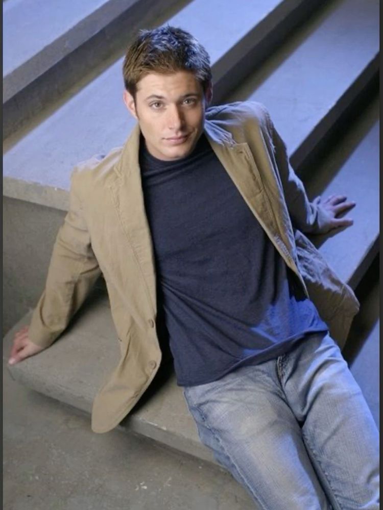 Jensen Ackles leaning back on a table 