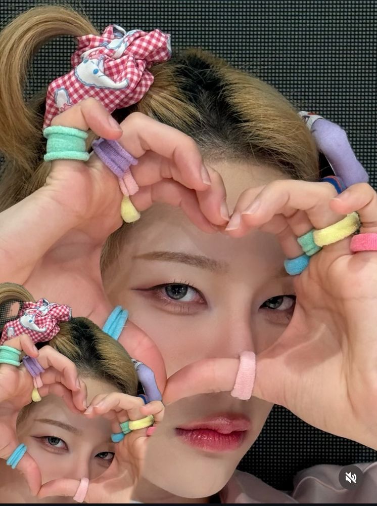 Rui making a hand heart to the camera. He’s wearing pastel rings on every finger and has a couple of cute hair accessories