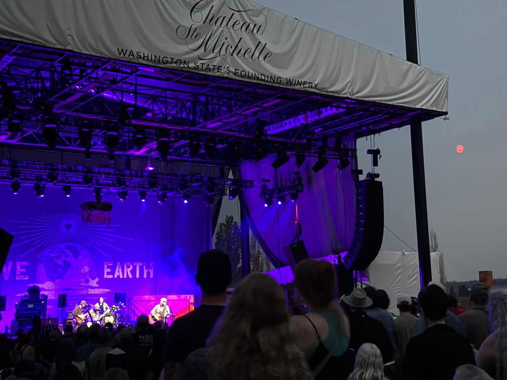 Neil Young on stage with an orange ‘harvest moon’ above right. 
