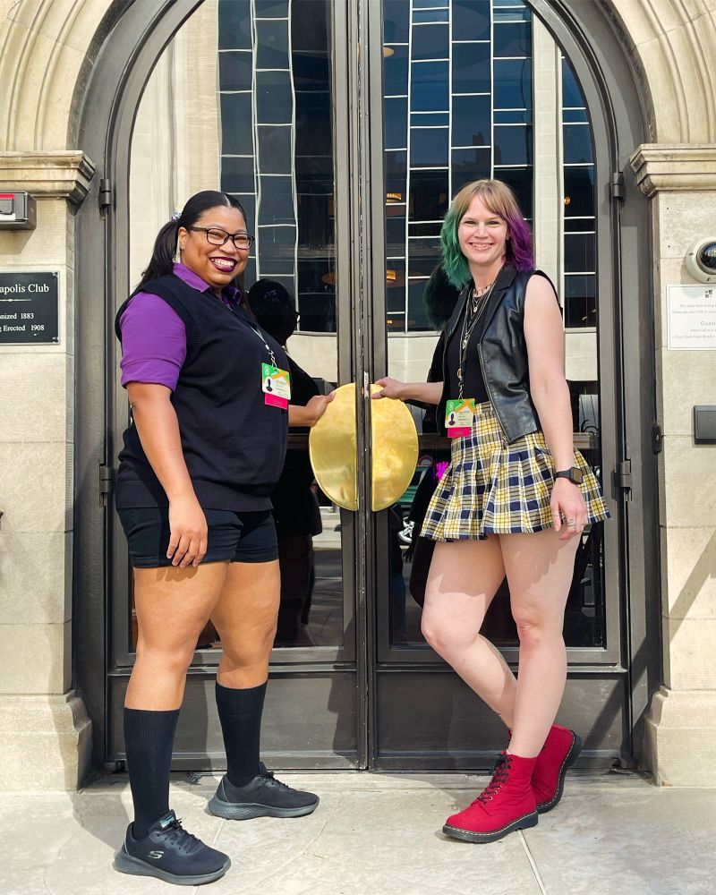 Two women standing on either side of double doors holding the handles, ready to open. Looking at the camera and smiling. 
