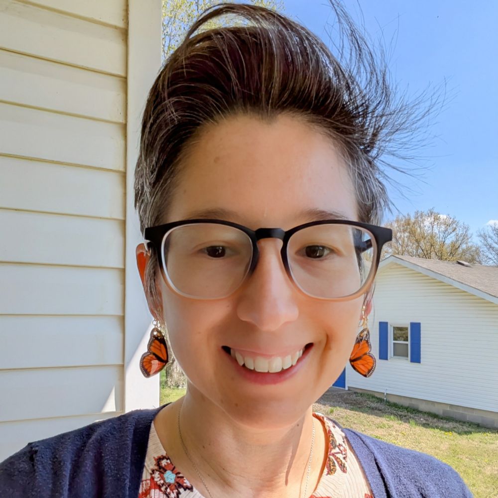 Selfie of me wearing my hand painted shrink plastic earrings in the style of monarch butterfly wings.
