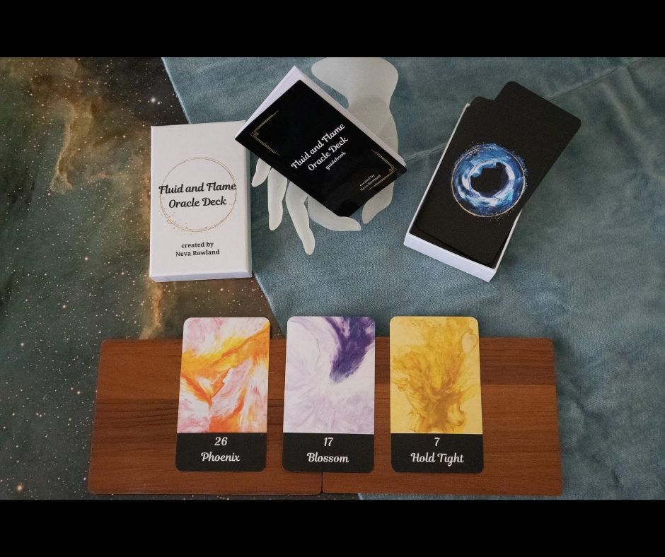 Photogenic view of my oracle deck. Three cards are laid out on a wooden board: Phoenix, Blossom, and Hold Tight. 