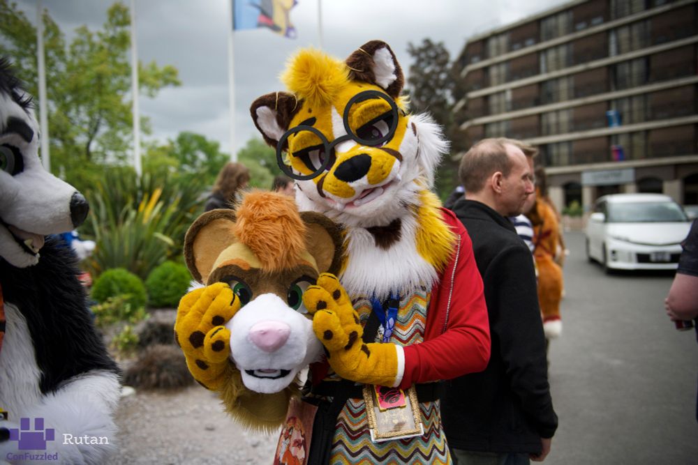 Me outside the front of the Hilton at cfz, in cheetah fursuit and dress, holding Marzi's head in my paws