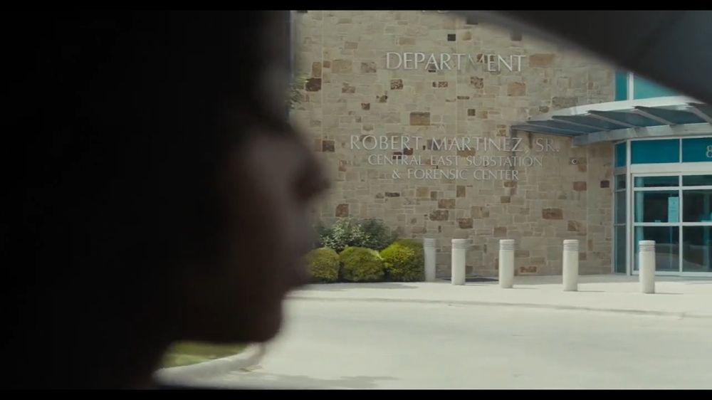 Colored image from the movie Test Pattern: Renesha Bell (played by Brittany S. Hall) drives by the forensic center of her city. We can see the silhouette of the side of her face, her eyes are looking down. 