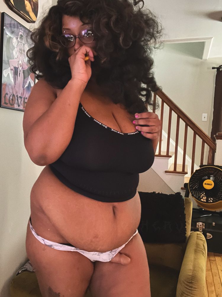 selfie of Lilith in a black tanktop and black and white thong with big curly hair, the photo is blurry and one hand is on her chest and the other is lifting up toward her mouth 