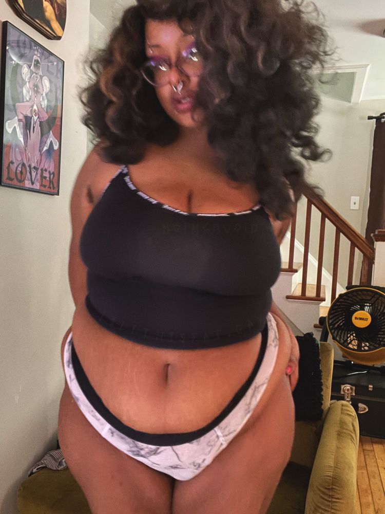 selfie of Lilith in a black tanktop and black and white thong with big curly hair, the photo is blurry and her hands are on her hips 