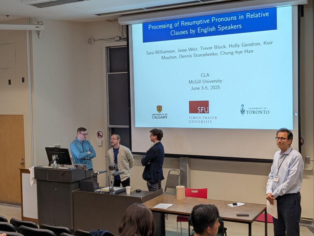 Four academics standing behind a podium at the front of a university classroom. The projector screen behind them shows a slide titled "Processing of Resumptive Pronouns in Relative Clauses by English Speakers".