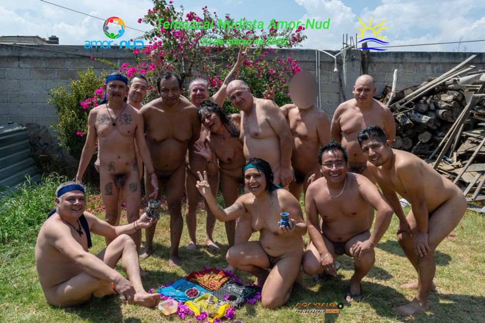 Twelve nude people on a lawn, in various poses.  The picture has the Amor-Nud logo, the Naturist Symbol, and the legends "Amor-Nud Nudist Temazcal" and "March 23, 2025".
