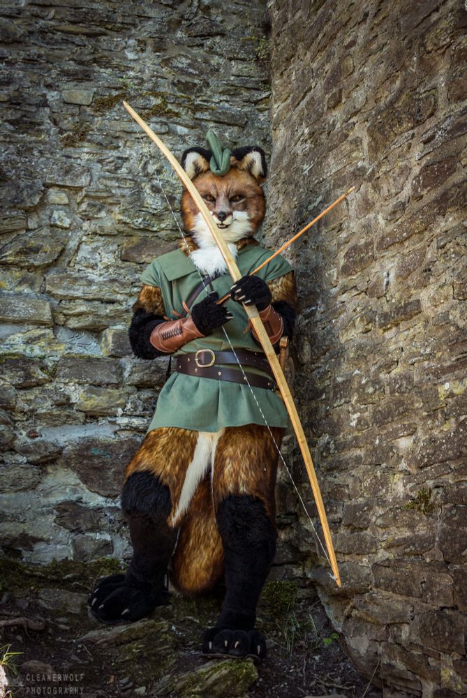 Realistic fursuit version of Robin Hood the fox with bow and arrow, ready to shoot. Robin is hiding behind a wall‘s ledge at a medieval castle.