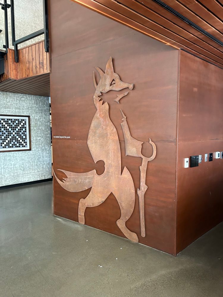 3m tall wall decoration/cafe logo depicting a digitigrade anthropomorphic fox with a walking stick. The fox is made of rusty iron.