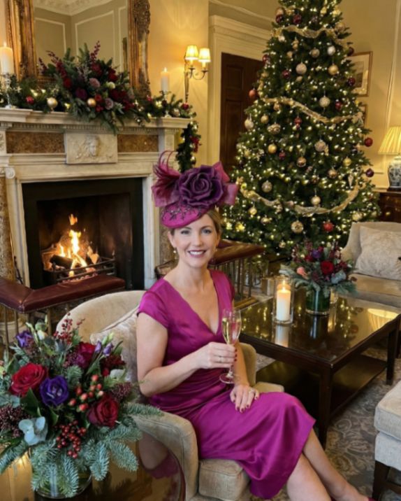 AI-generated lifestyle image used for inspiration only, showing the actual hat worn in a festive Christmas wedding setting with a tree, a fireplace and elegant décor. Helps visualise how the Mother of the Bride might style the fascinator on a winter wedding day.