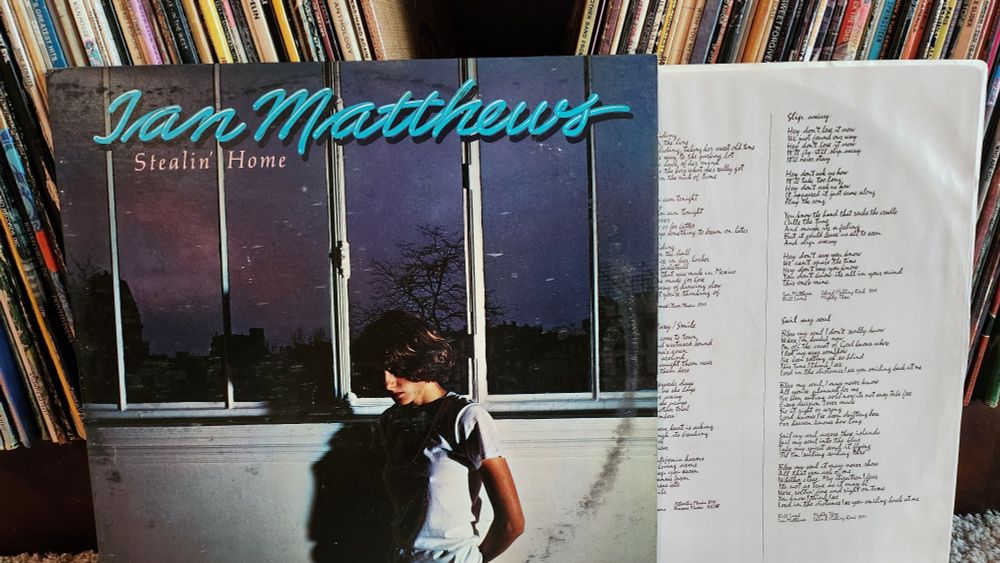 Album art: photo of a white man, looking down, standing in front of windows showing the night sky.