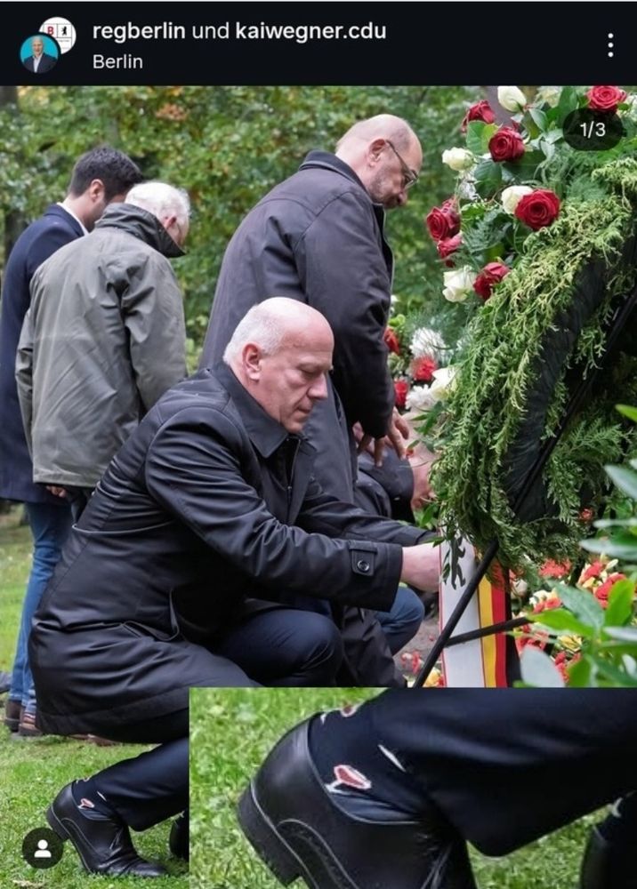 Kai Wegner kniet am Grab. Seine nach oben rutschende Hose offenbart eine Socke mit aufgedrucktem Rotweinglas.