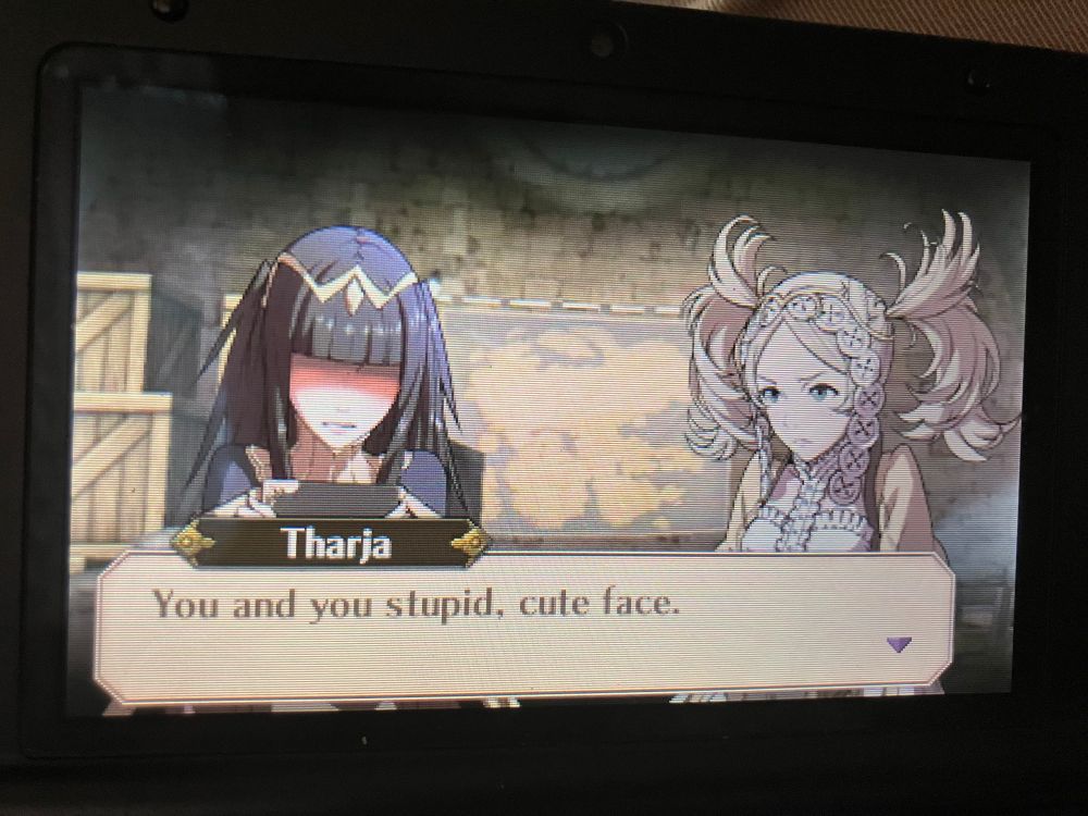 Tharja and Lissa from Fire Emblem Awakening. Tharja is blushing as she says “You and your stupid, cute face.”