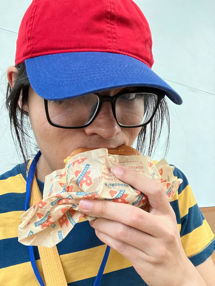 A picture of me, dressed up as Ness from Earthbound, eating a Double Cheeseburger from Burgerville.
