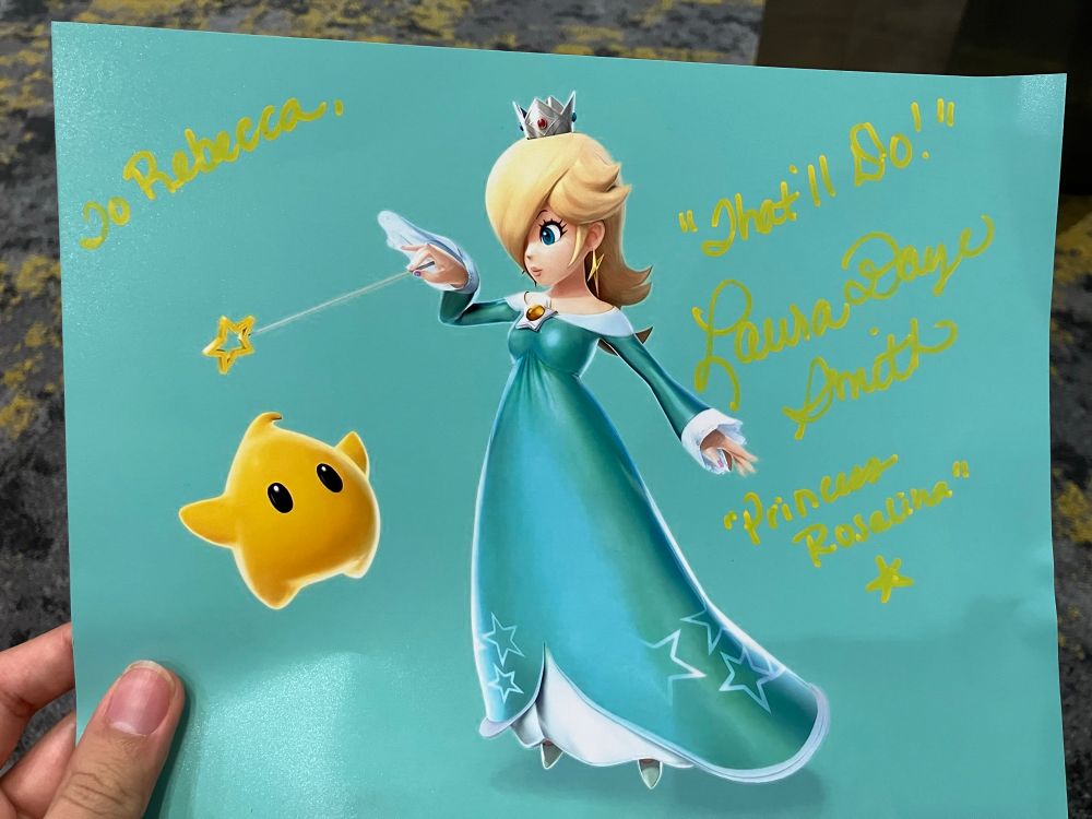 A picture of the 8x10 print i purchased from Laura Faye Smith. The text reads “To Rebecca, “That’ll Do!” Laura Faye Smith, “Princess Rosalina” “ with a render of Rosalina from Super Smash Bros 3DS / Wii U.