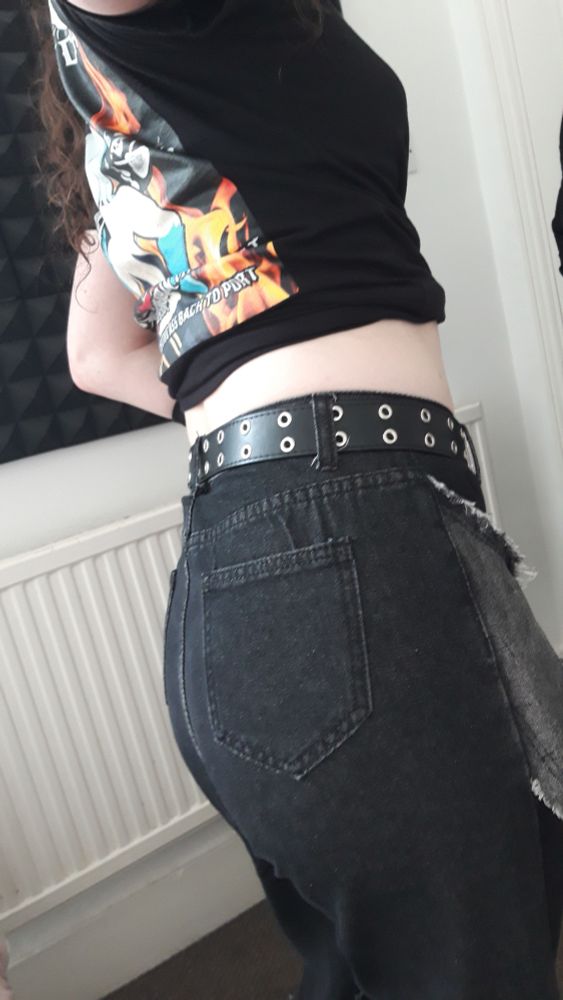 A selfie of Oceonax in a tied-off black shirt with Dandyfloss on the back, plus jeans, showing off her back.