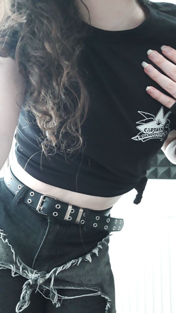 A selfie of Oceonax in a tied-off black shirt with Dandyfloss' logo on the front, plus jeans, leaning forward and showing off her curly brown hair.