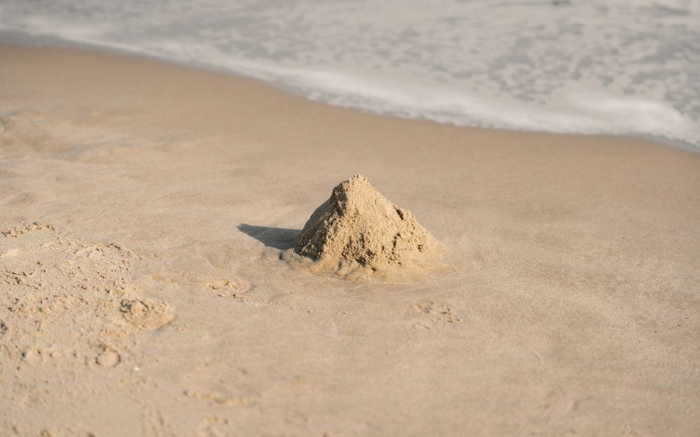 Un petit château de sable ridicule sur la place, avec la marée qui monte.