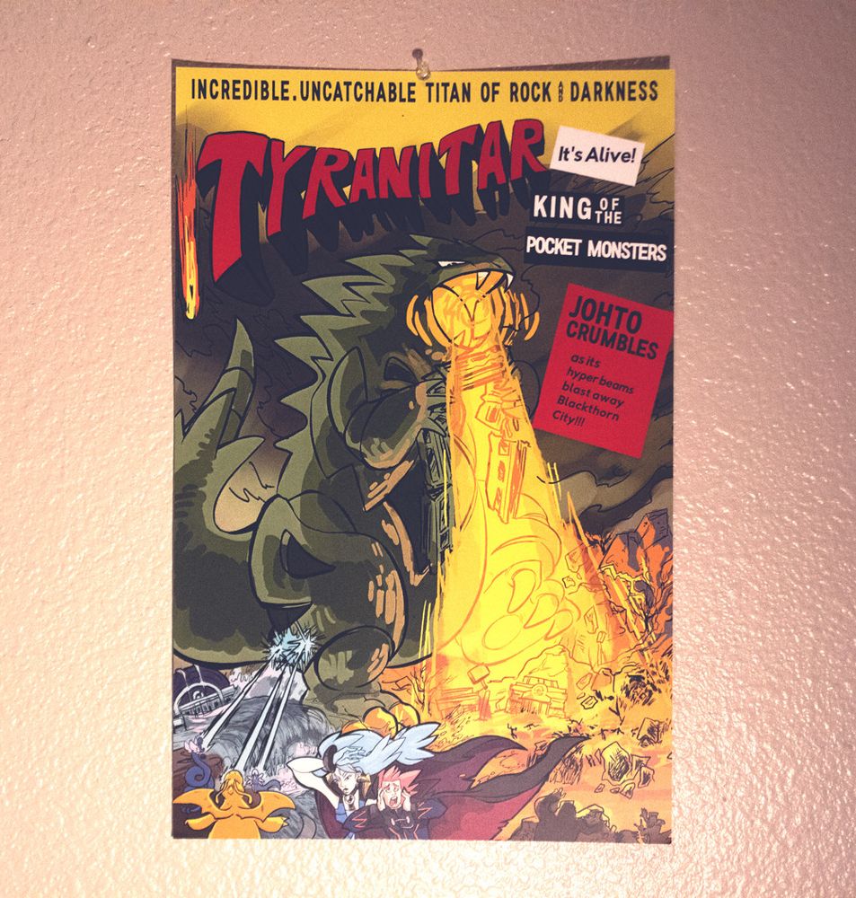 A Tyranitar x Godzilla parody poster featuring Tyranitar destroying Blackthorn City in Pokemon Gold / Silver with Lance and Clair the dragon tamers running away in the foreground. Behind them, the Pokemon Center is being obliterated while dragon Pokemon attempt stopping the beast blasting hyperbeams.

"Tyranitar - it's alive! - King of the Pocket Monsters - Johto Crumbles at its hyper beams blast away Blackthorn City!"