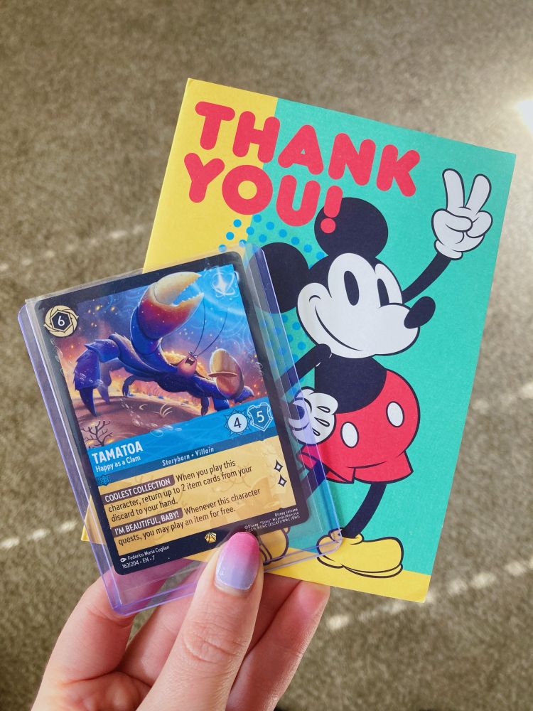 A Disney Lorcana card called Tamatoa - Happy as a Clam, and a Thank You card with Mickey Mouse on it. 