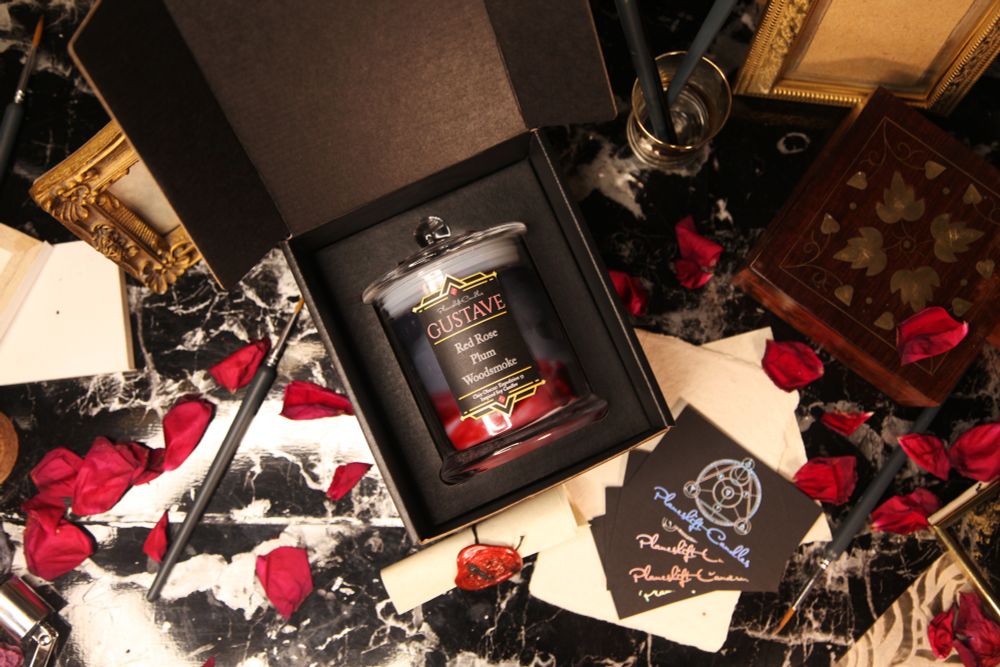 A black, grey and red candle in a clear glass jar is secured in a black card box
