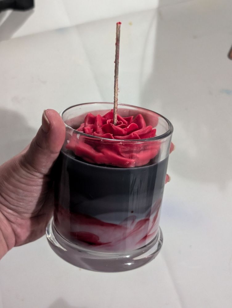 A black, grey and red candle with a red wax rose on top. 