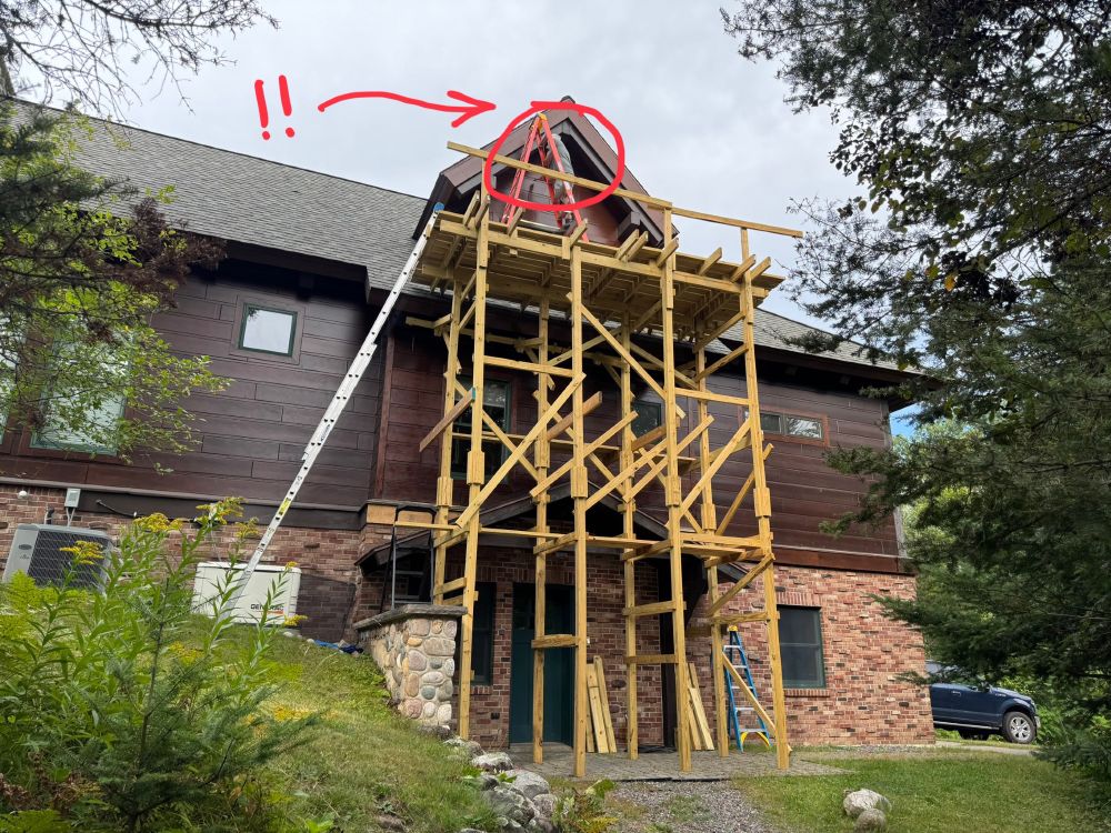 A clearly insane man is standing on a ladder, which is on top of a three-story scaffold. This man’s wife is not pleased.