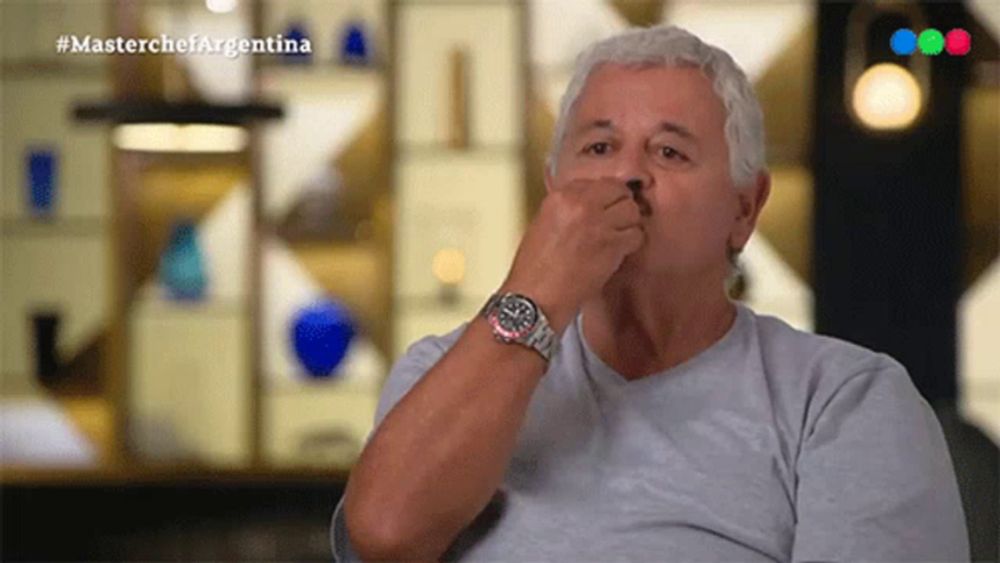 a man wearing a watch holds his nose while watching a masterchef argentina show