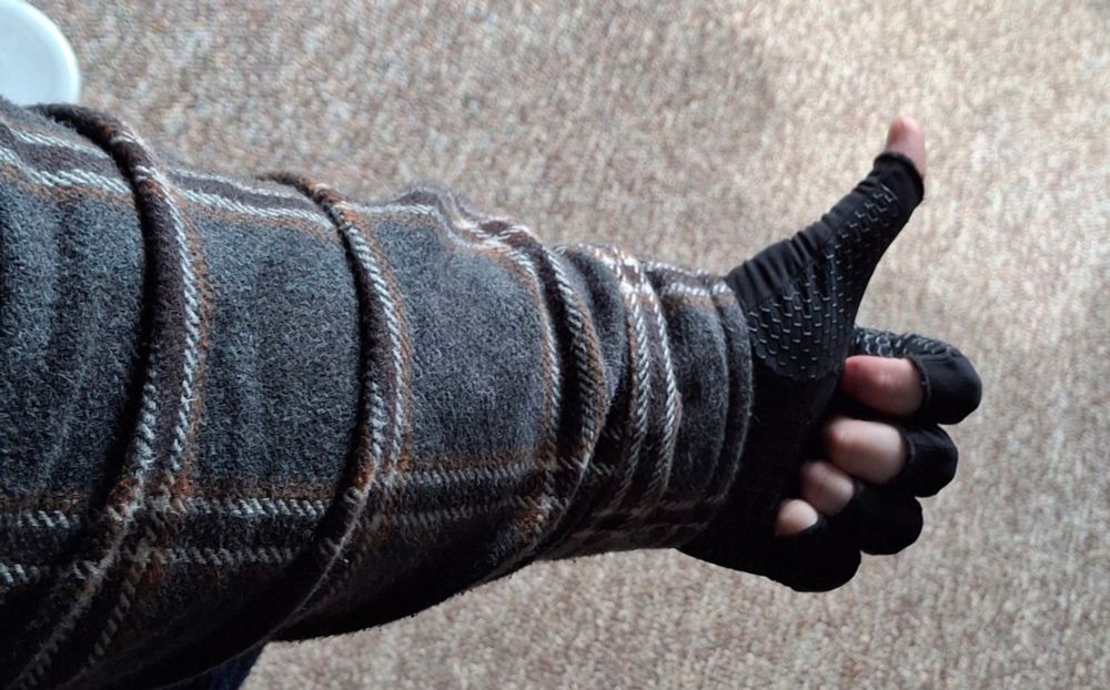 My arm in a long sleeve flannel shirt and compression gloves giving a thumbs up.