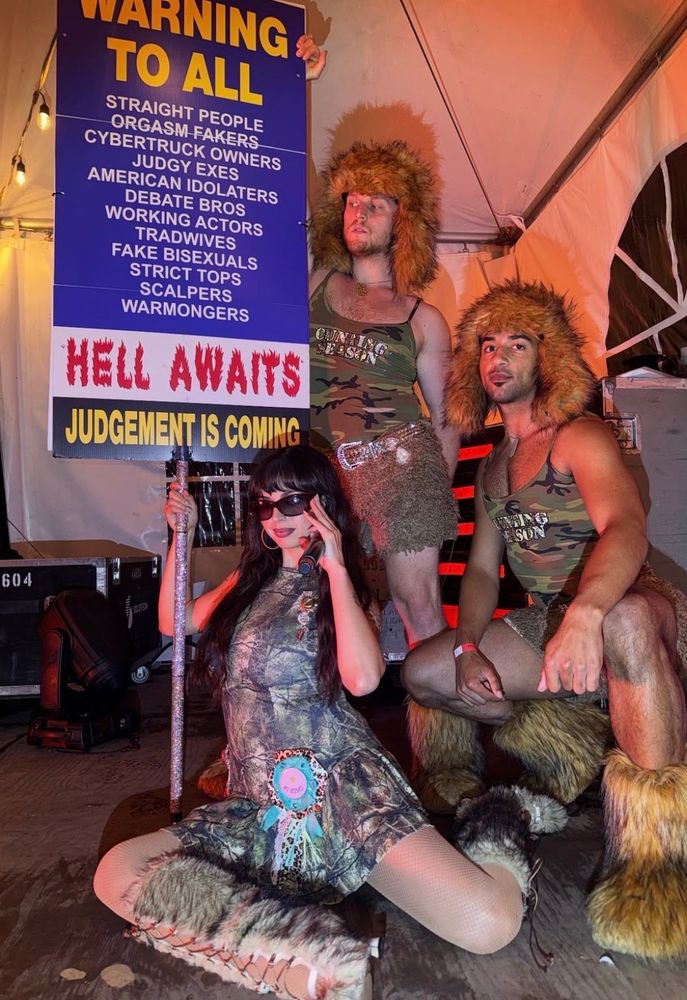 rebecca black muito linda com dois dançarinos apetitosos. ela segura uma placa que chama por todos os “comportamentos” que ela julga errados e diz que o inferno aguarda.