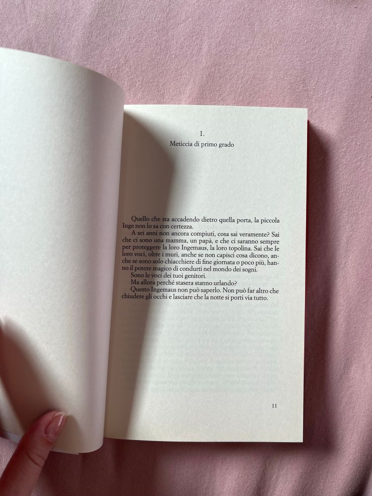 Erste Textseite:
1. Meticcia di primo grado
Quello che sta accadendo dietro quella porta, la piccola Inge non lo sa con certezza.
A sei anni non ancora compiuti, cosa sai veramente? Sai che ci sono una mamma, un papà, e che ci saranno sempre per proteggere la loro Ingemaus, la loro topolina. Sai che le oro voci, oltre i muri, anche se non capisci cosa dicono, anche se sono solo chiacchiere di fine giornata o poco più, hanno il potere magico di condurti nel mondo dei sogni.
Sono le voci dei tuoi genitori.
Ma allora perché stasera stanno urlando?
Questo Ingemaus non può saperlo. Non può far altro che chiudere gli occhi e lasciare che la notte si porti via tutto.