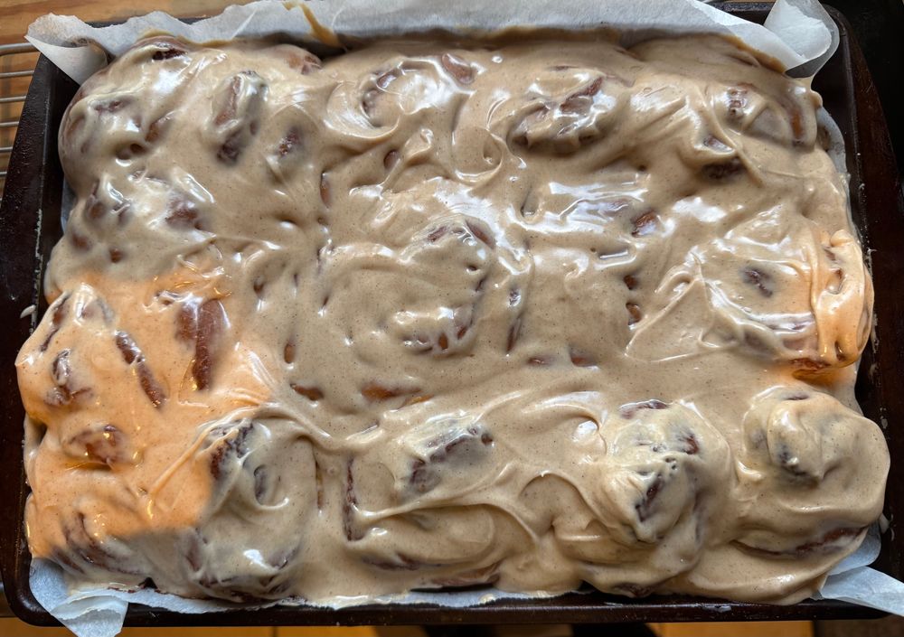 Aerial view of cinnamon cream cheese frosting swirled onto a tray of cinnamon rolls